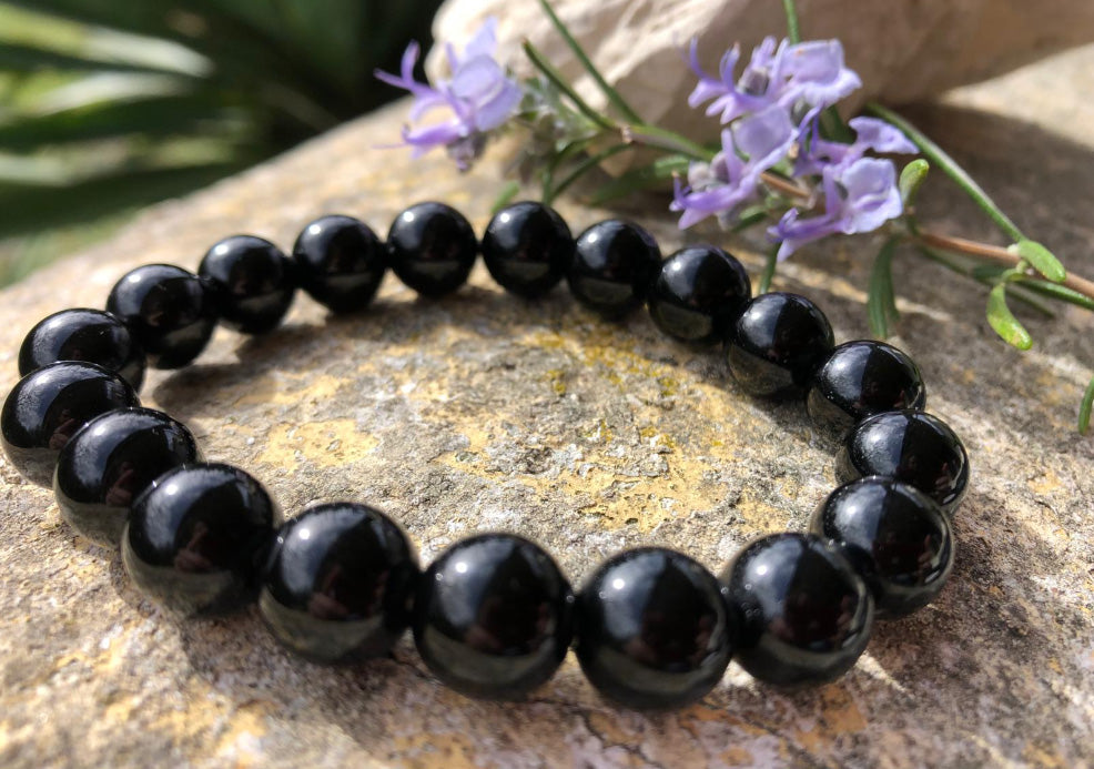 Bracelet en Obsidienne noire posé sur un rocher devant des fleurs violettes
