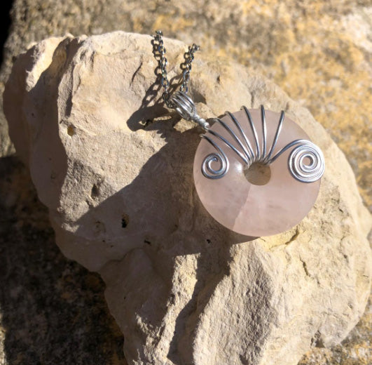 Colllier Donut en Quartz Rose et métal argenté posé sur une Pierre