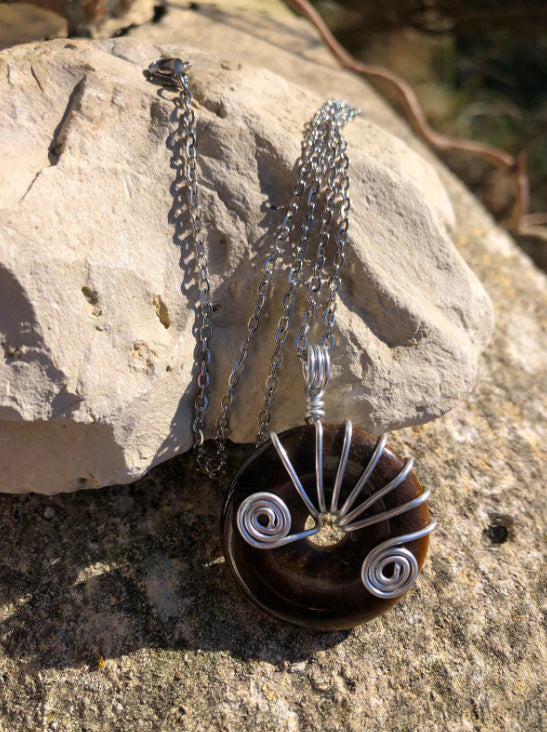Collier donut en pierre Oeil de Tigre et métal argenté posé sur une pierre