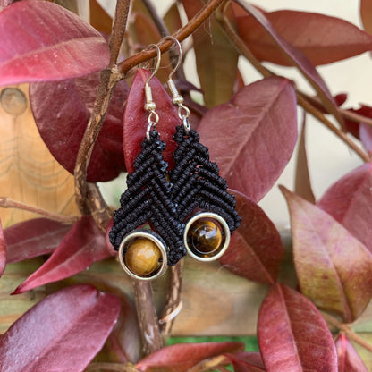 Boucles d’oreilles bohèmes en micro-macramé noir avec perle d’œil de tigre, symbole de protection et d’assurance féminine.