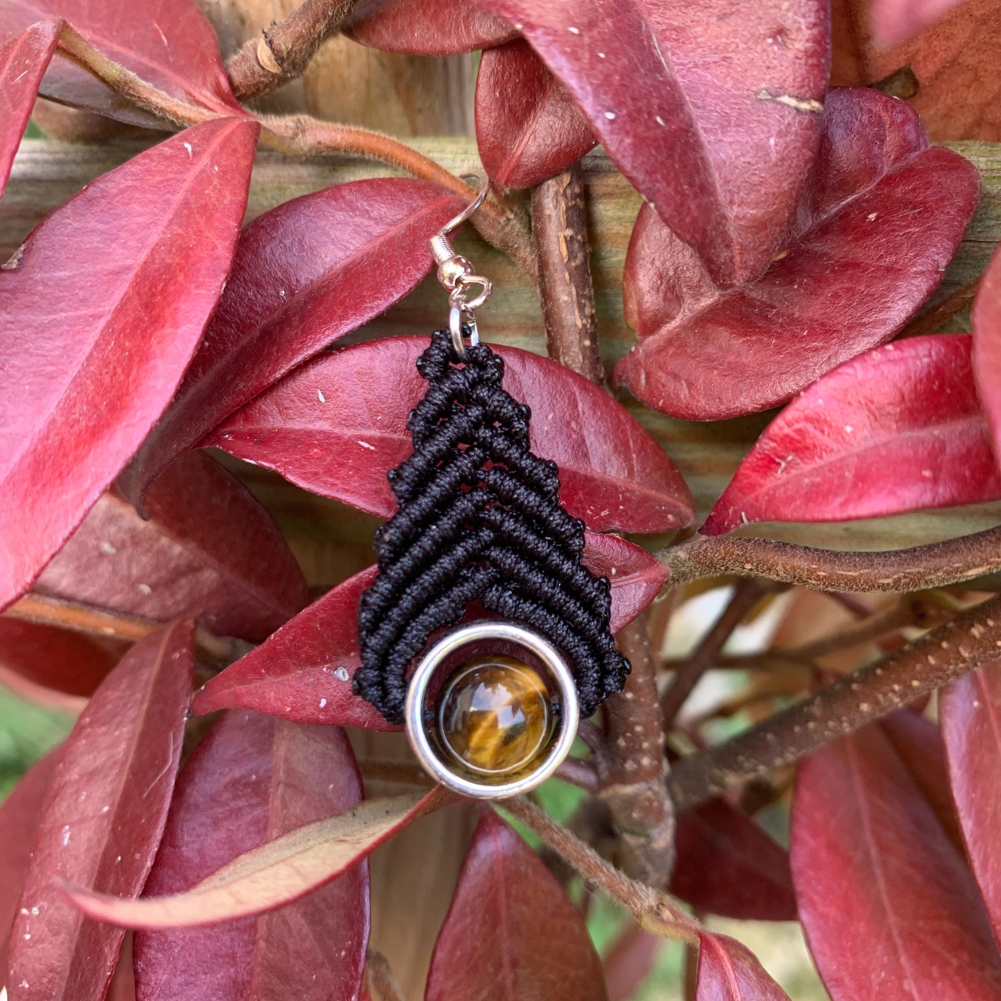 Bijou artisanal fait main en macramé noir et pierre naturelle œil de tigre, photographié dans un style bohème chic.