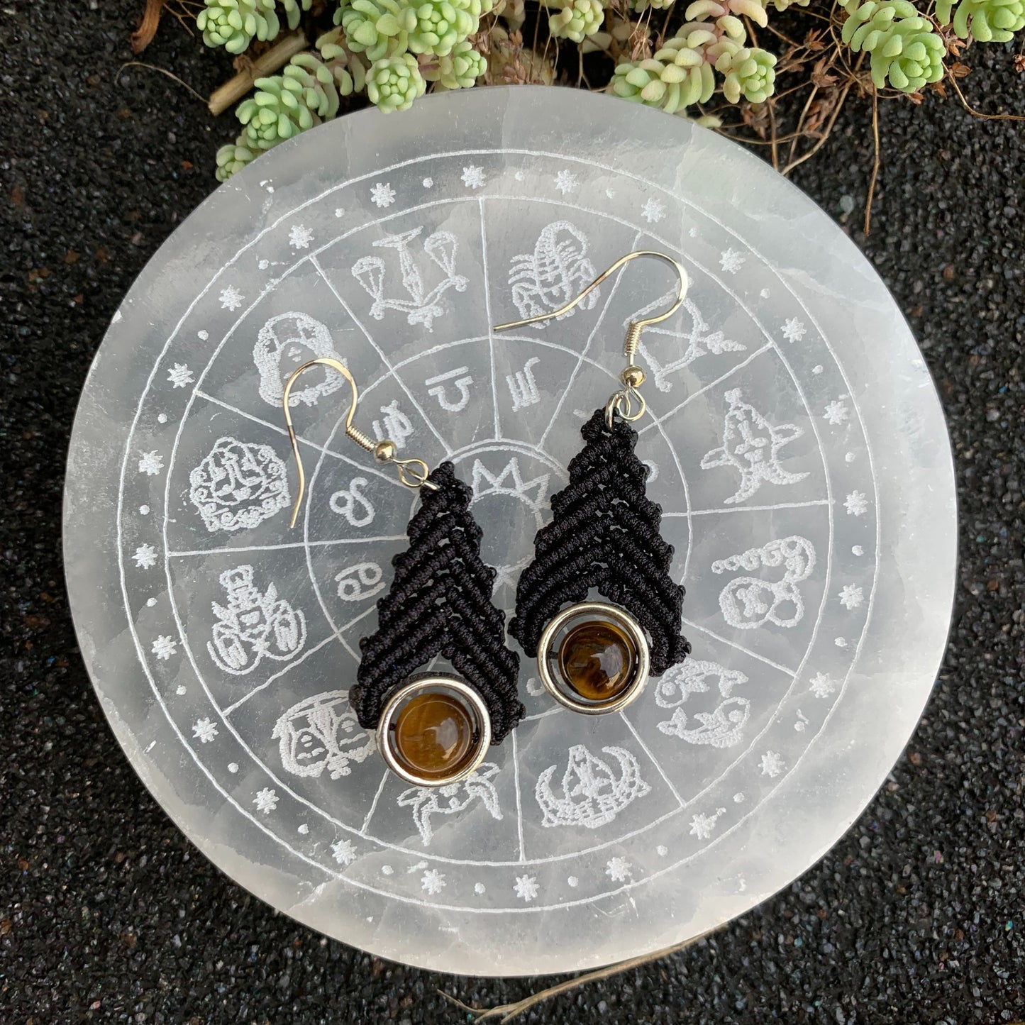 Boucles d’oreilles en macramé noir ornées d’une perle d’œil de tigre, accessoire bohème aux vertus de confiance et d’ancrage.