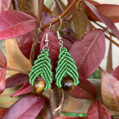 Boucles d’oreilles artisanales en micro-macramé et perles d’œil de tigre posées sur des feuilles d’automne, symbole d’ancrage et de protection.