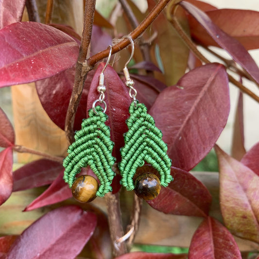 Boucles d’oreilles artisanales en micro-macramé et perles d’œil de tigre posées sur des feuilles d’automne, symbole d’ancrage et de protection.