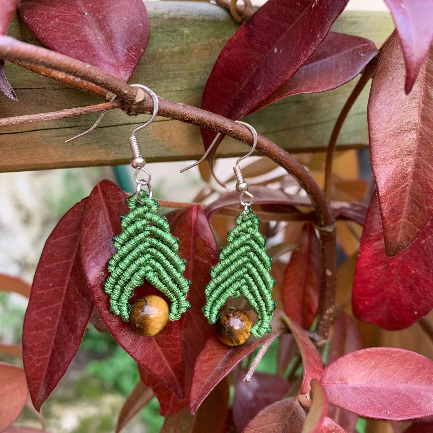Boucles d’oreilles en micro-macramé avec perles de lithothérapie en œil de tigre, capturées dans un décor automnal aux teintes rouges et cuivrées.