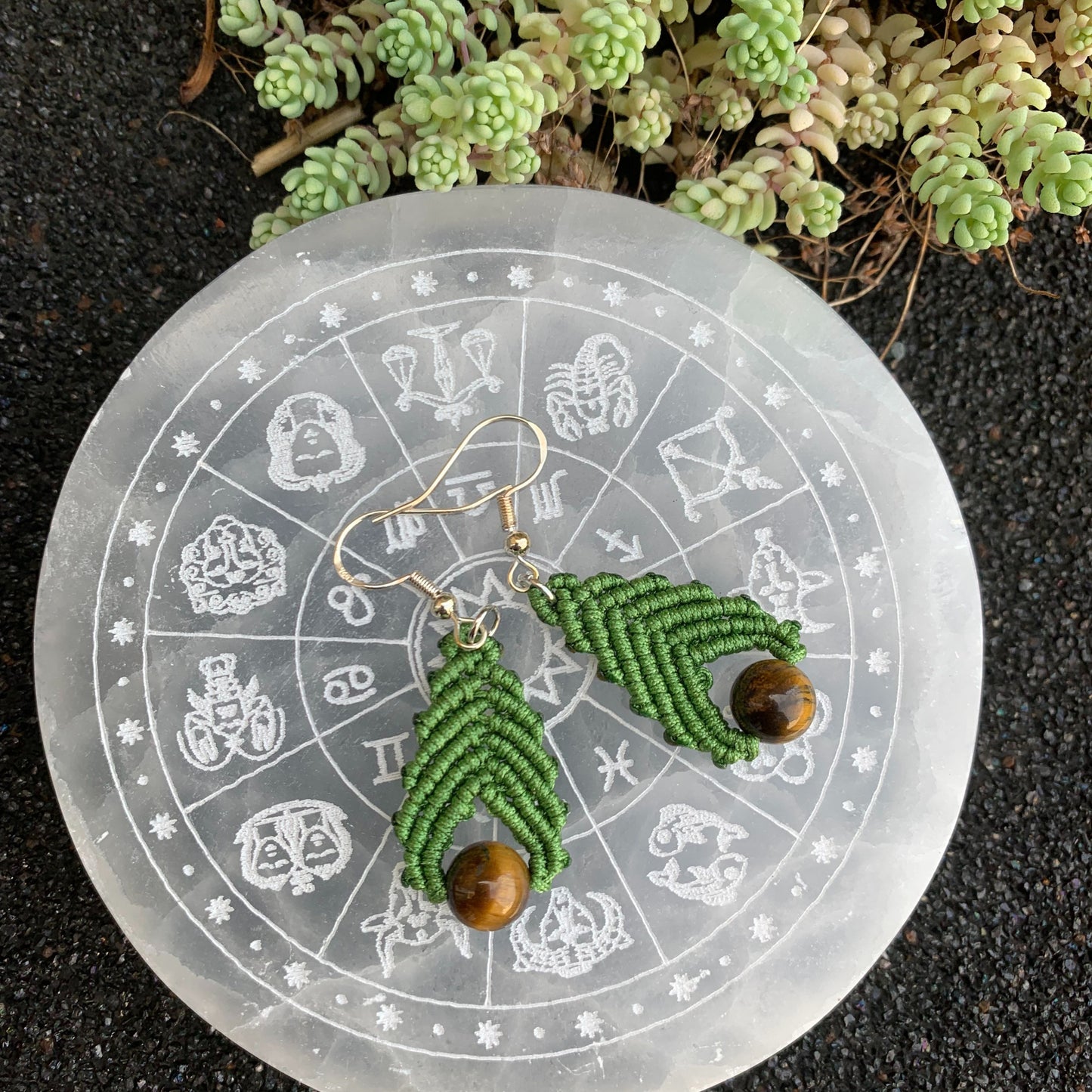 Création artisanale en micro-macramé ornée de pierres d’œil de tigre, mise en scène sur un disque en séléntite évoquant la transformation et la sérénité.