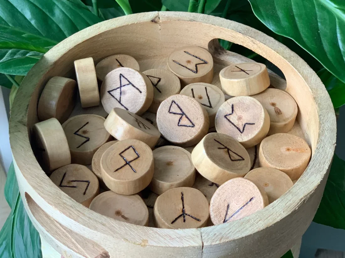 Runes du Futhark ancien pyrogravées dans des rondelles de cerisier, rangées dans un bol en bois